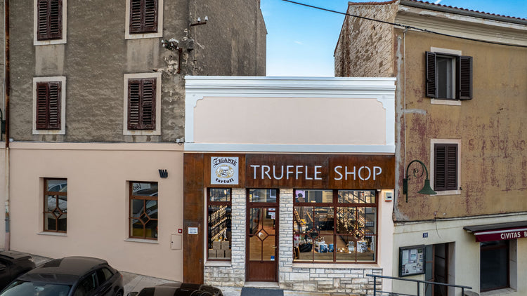 A storefront building labeled "TRUFFLE SHOP" with large windows, a beige facade, and a rustic stone-and-brick entrance, photographed on a street with neighboring buildings and parked cars.